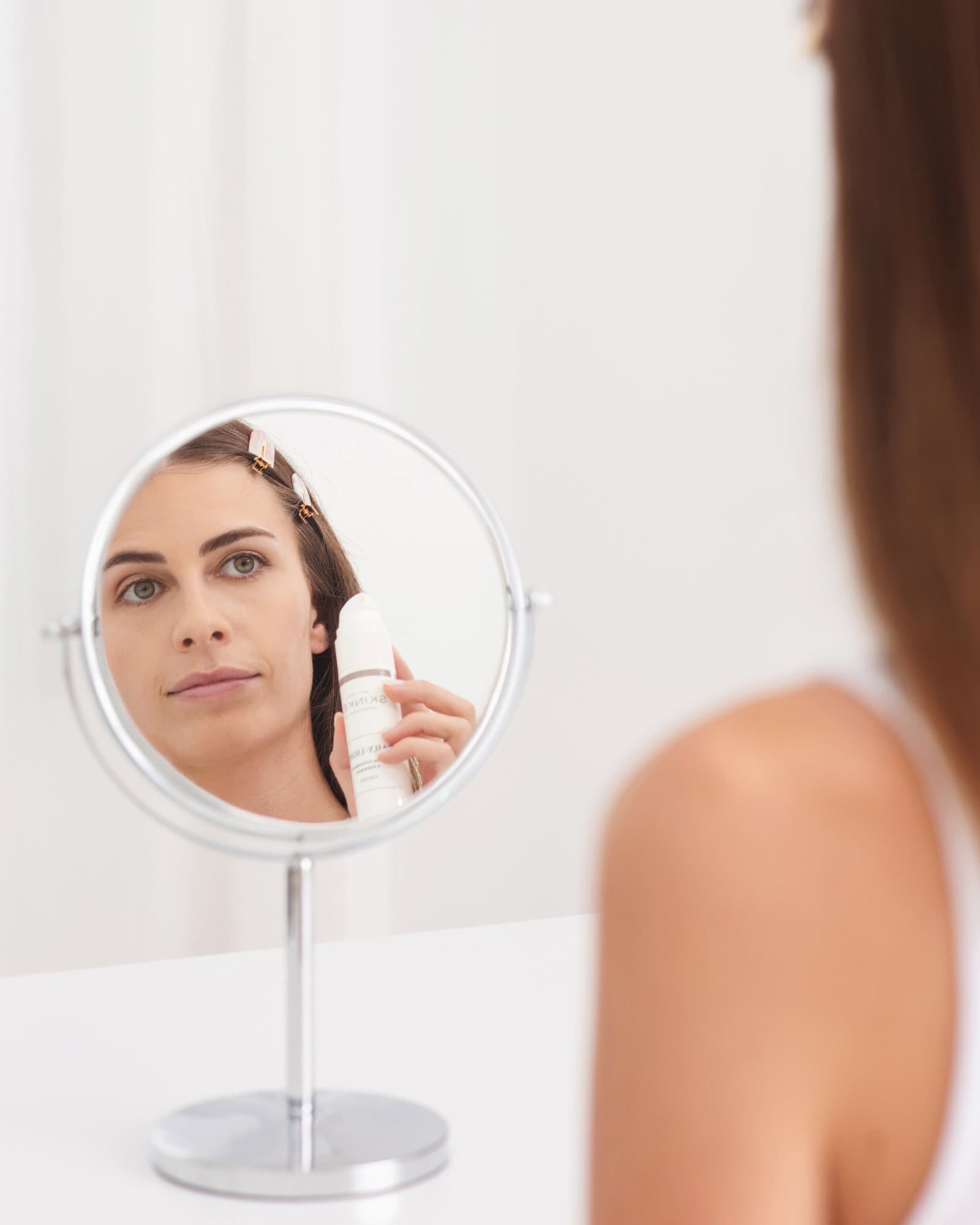 Mujer mirándose en un espejo con un producto Skinkel