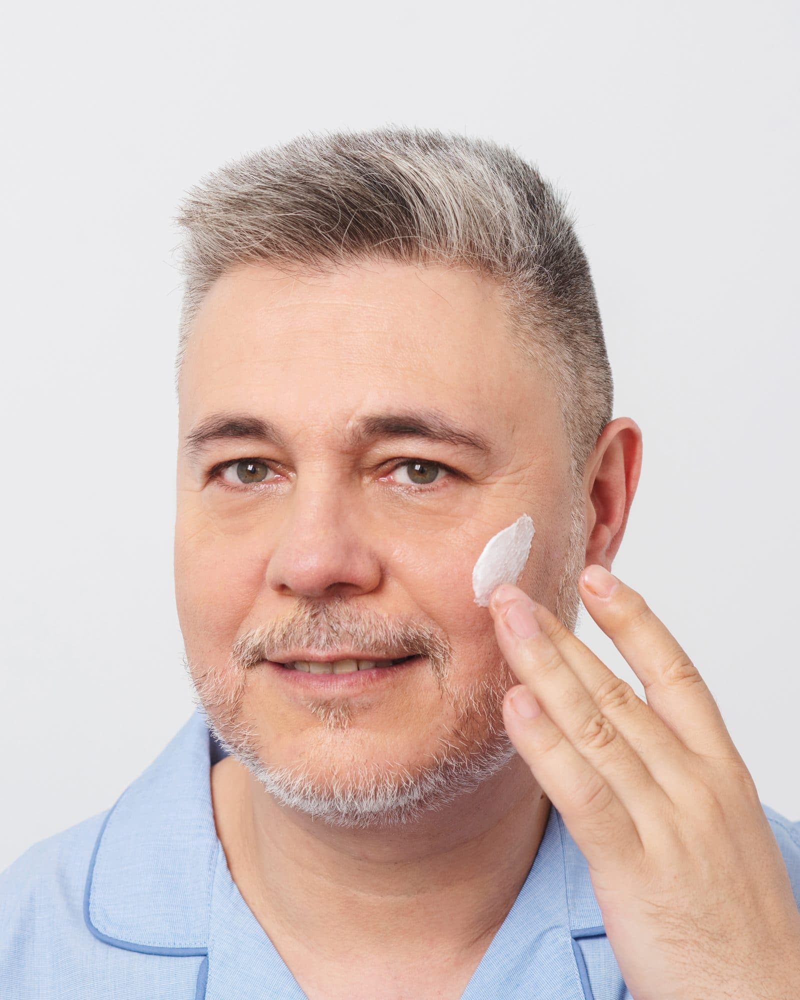 Hombre de mediana edad aplicándose crema en la mejilla